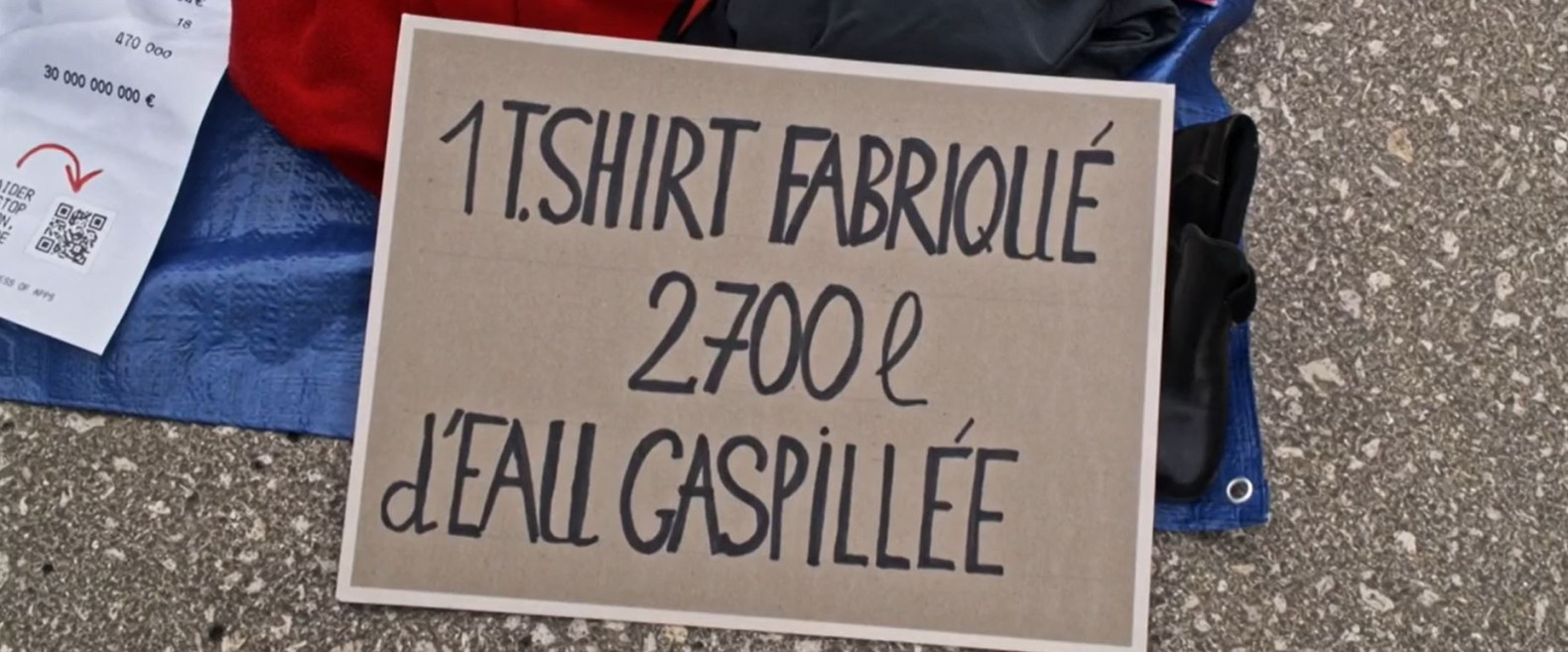Une pancarte sur laquelle il est écrit : « un T-shirt fabriqué 2 700 litres d'eau gaspillée »
